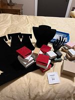 Full assortment of black velvet jewelry display stands for necklaces and bracelets, black hand-shaped stand, and multiple small jewelry packaging boxes in various colors and sizes set on a beige cloth surface.