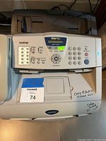 Front view of Brother MFC-7220 laser printer showing control panel, keypad, and display screen. Visible notes indicate toner cartridges included.