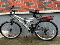 Full side view of the silver Supercycle men's mountain bike showing frame, wheels, seat, pedals, and rear rack.