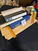 Photo of office supplies including large manila envelopes, two binders, wall-mounted metal pencil sharpener, two wooden rulers, and a desktop stapler.