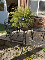 Four black metal outdoor bistro chairs arranged outside with visible rust and wear on surfaces.