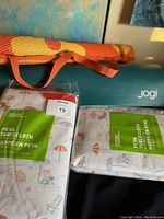 Rolled orange and yellow patterned beach mat with orange straps and two PEVA plastic tablecloths featuring a beach chair and umbrella print in pastel colors.