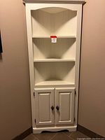 Full front view of a white painted pine corner cabinet showing three open shelves and two-door storage below