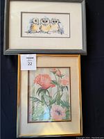 Photo showing two framed artworks: bird print on top with gray frame, flower watercolour painting below with gold frame.