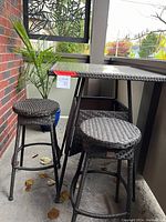 Photo of patio bistro set showing high top rectangular table with glass top and two tall stools with woven seats in a balcony setting.