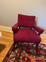 Front view of magenta retro armchair showing cushioned seat, backrest with two buttons, and padded armrests.