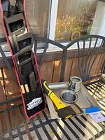 Set showing three saws in black plastic handles stored in a Jobmate carrying case next to a yellow and black hatchet and a metal fire dish with small metal containers on a black metal chair outdoors.