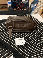 Brown Fossil leather toiletry bag resting on black and white patterned blanket scarf