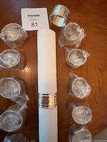 Twelve silver plated napkin rings arranged on a wooden surface with a white paper towel inside one ring.
