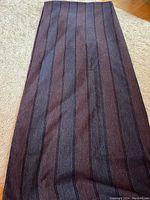 Photo of length of blue and purple striped fabric laid out on a light colored shag carpet showing vertical stripes and color pattern.