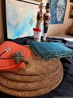 Round brown beaded placemats, orange rubber placemats stacked, blue textured table cloth, and two carved wooden pilgrim candle holders standing behind them.