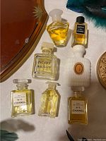 Close-up of six vintage perfume bottles with various labels, glass stoppers, and colored contents.