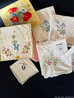 Full view of the various embroidered linen pieces arranged together showing different floral designs and colors.