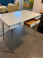 Photo of a vintage kitchen table with a light speckled laminate top, visible small drawer open on the right side, and chrome metal legs.