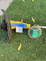 Yellow electric weed whacker with guard is shown laying on grass with nearby spool of Weed Eater trimmer line in packaging.
