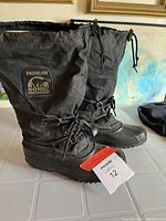 Pair of tall black Sorel Snowlion winter boots shown standing upright, displaying exterior details including lace and drawstring closures