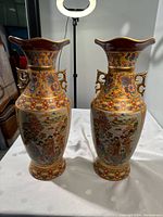 Front view of the pair of Asian porcelain vases showing colorful hand-painted scenes and decorative handles.