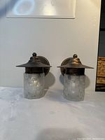 Front view of two outdoor wall light fixtures showing bronze finish and mosaic glass shades.