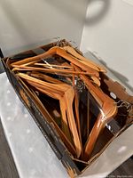 Box containing 31 wooden clothes hangers with metal hooks, showing natural wood finish and classic design for clothing support.