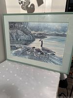 Framed print of Canadian geese by rocky water shoreline with pale green frame and double mat.
