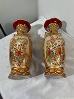 Pair of Asian porcelain vases with intricate painted figurative and floral decorations, shown upright on a white cover