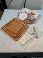 Photo showing the three square bamboo trays stacked flat, the round cheese tray, plus assembly hardware and instructions on a white table.
