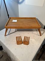 Photo showing bamboo breakfast tray with legs extended placed on tablecloth with two bamboo salad tongs in front.