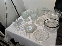 Table showing large assortment of clear glass bowls, cups and plates with different patterns and textures, no damage visible.