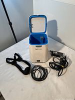SoClean CPAP cleaner open unit with blue interior and included black strap and power adapter on a table.