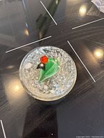 First glass paperweight resting on reflective black surface, showing green leaf with red ladybug inside clear glass with bubbles and accents.
