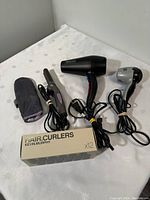 Full view of the lot with all items displayed: two hair dryers, hair straightener, Kevin Murphy hair curlers box, and heat-resistant glove.