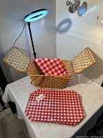 Woven picnic basket opened with red and white checkered tablecloth and placemats inside and in front.