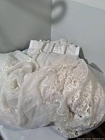 Photo of three cream pleated sheer curtains with ornate floral embroidery laid out showing fabric texture and design detail.