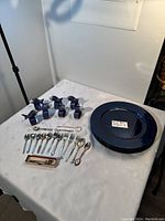 Photo showing the full set on table including 8 blue charger plates, 6 fish-shaped napkin rings, 7 small spoons, 7 small forks and boxed tea strainer spoon.