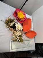 Photo showing colorful nested plastic bowls and trays, and glass tray on a table, with artificial flowers