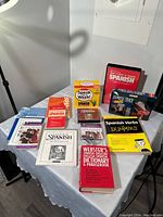 Photo of entire lot showing variety of Spanish language learning books and audio materials arranged on table against gray wall