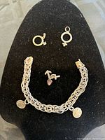 Sterling silver charm bracelet with woven chain and two round charms, along with three separate gender symbol charms placed on black display.