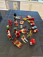 Photo showing a spread of colorful wooden Christmas ornaments on a black surface. Includes Santas, reindeer, toy soldiers, sleds, and a gramophone among other festive figures.