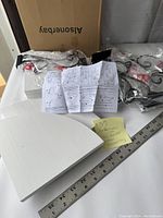 Contents of new open box showing four white corner wood shelves, wrapped metal cat-shaped brackets, assembly hardware, and instruction sheets on a table.