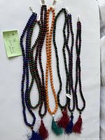 Seven strands of glass bead necklaces laid out with price tags and tassels visible.