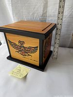 Front and side views of bentwood box showing Native art with bird motif and artist signature on side panel and black framing around panels. Includes measuring ruler showing dimensions and sticky note with lot info.