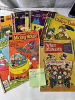 Lot of 12 Walt Disney comic books arranged overlapping on a white surface showing front covers including Mickey Mouse, Daisy Duck, Chip 'n Dale, Goofy, and others.