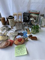 Photo showing a variety of items including German beer stein, pewter flask, belt buckles, small green glass bottles, figurines, and assorted pins and coins.