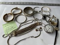 Lot of vintage jewelry including pocket watches, various bracelets and bangles, small earrings or cufflinks, placed flat with a measuring ruler for scale