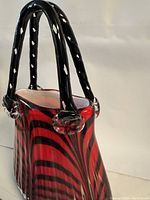 Side angled view of the red and black tiger stripe blown glass vase shaped like a purse with black twisted glass handles.
