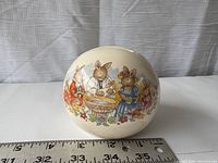 Round ceramic money bank decorated with Royal Doulton Bunnykins bunny family scenes around a christening.