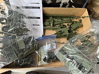 Open box with sprues of olive green plastic parts, several loose bags containing model pieces, and instruction manual partially visible