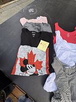 Photo of folded tank tops, a Mickey Mouse graphic T-shirt, and other clothing items to show variety and condition of lot