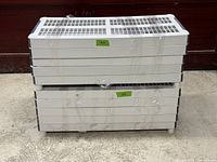 Two sets of white plastic shelving units disassembled flat and stacked, plastic wrapped for transport.