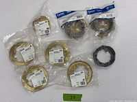 Photo showing 4 Hubbell 6230 brass round carpet flange plates in sealed packaging, 1 Hubbell 6249 brass duplex cover with lift lids in sealed packaging, and 3 Carlon floor box adapter rings (two sealed, one loose) arranged on a flat surface.